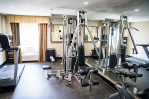 Een sportschool met cardioapparatuur, krachtapparaten en een spiegelwand.