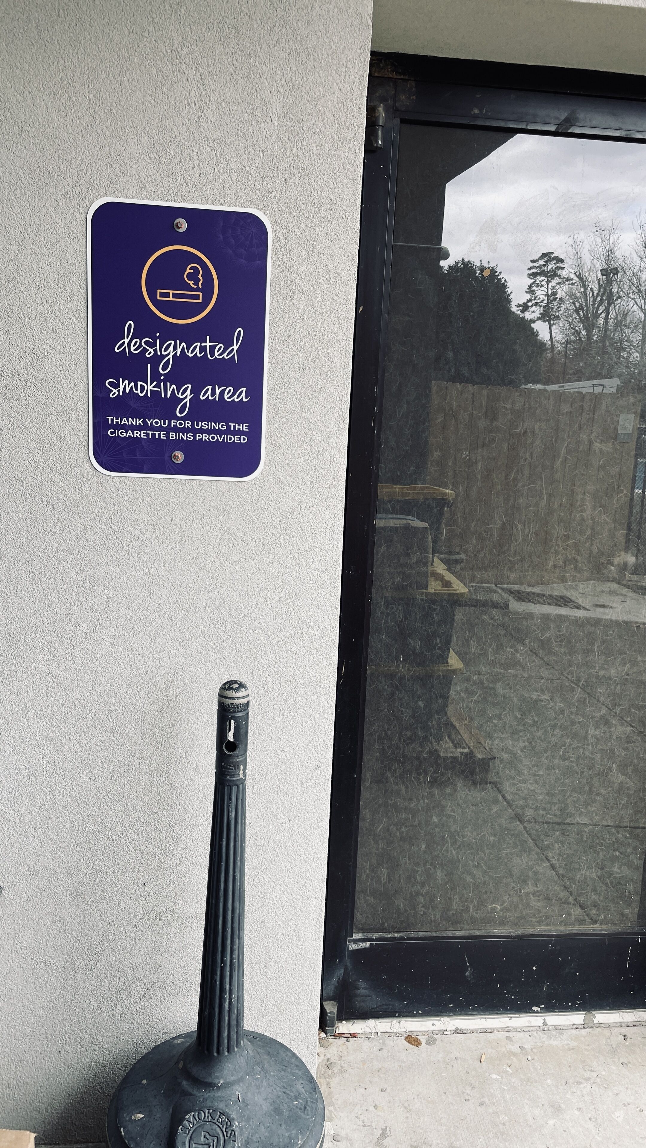 Un panneau indiquant la zone réservée aux fumeurs et un tuyau métallique fixé au mur.