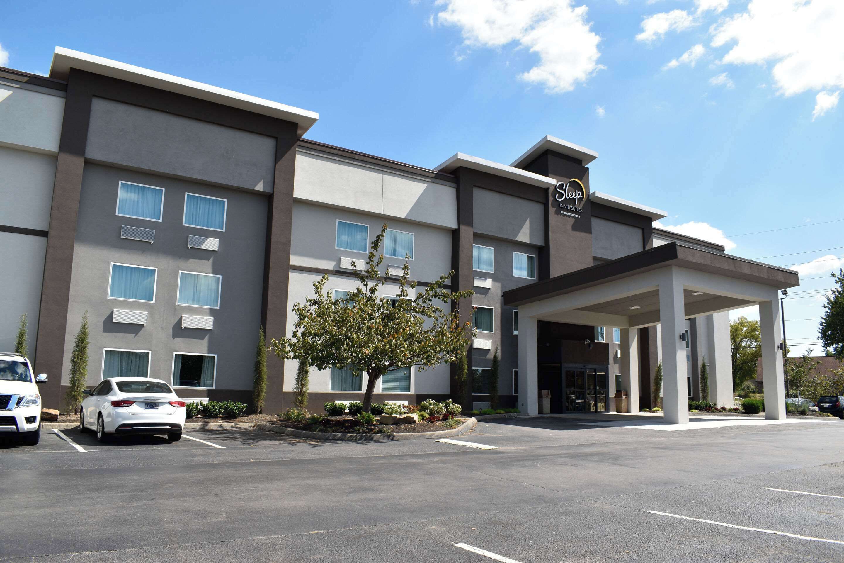 A modern hotel with a covered entrance, multiple windows, and a parking lot.