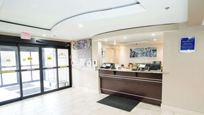 Een hotel receptie met een modern design, met een receptiebalie, een digitaal scherm en een wandkunstwerk.