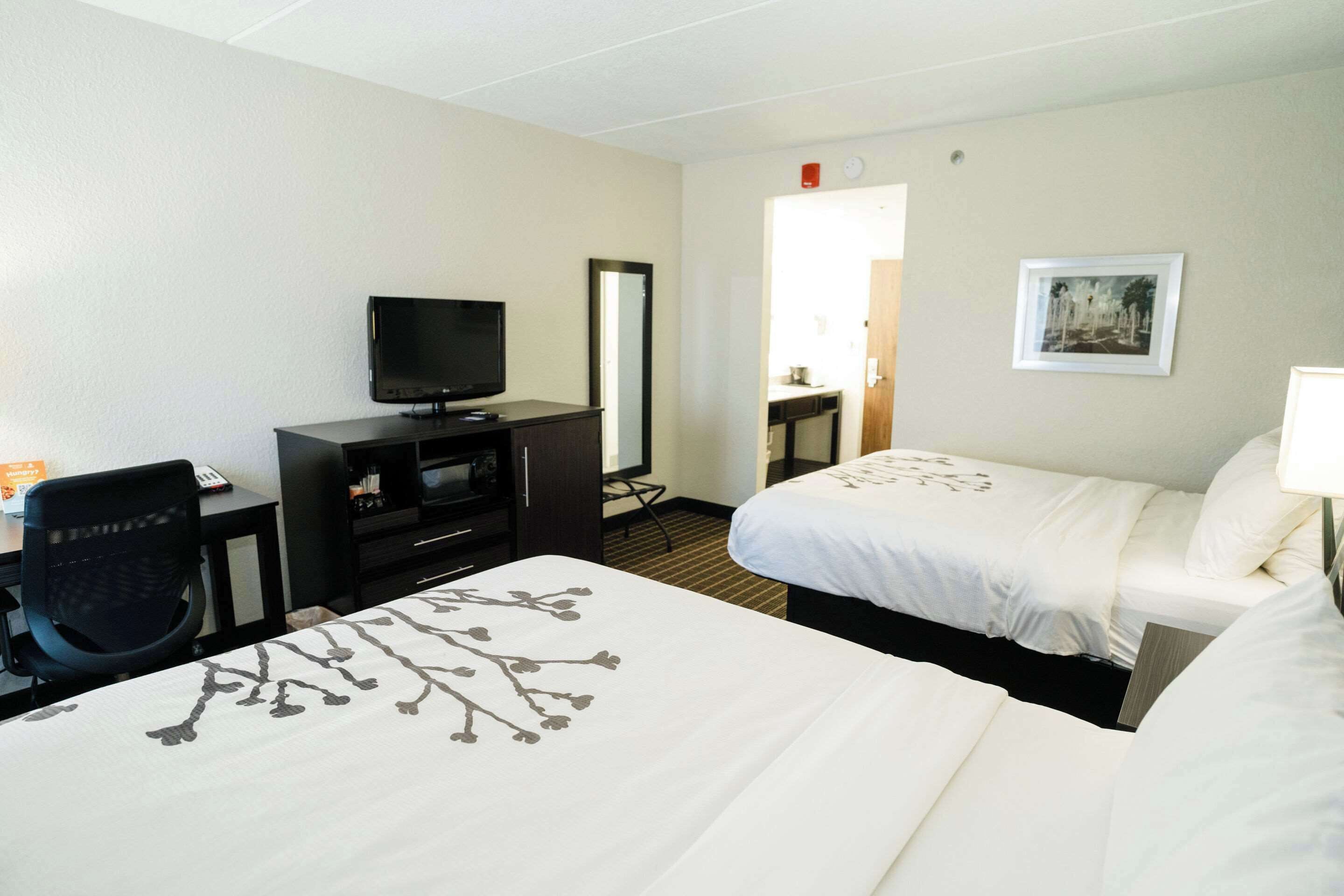 A hotel room with two beds, a desk with a television, a chair, and a small cabinet.