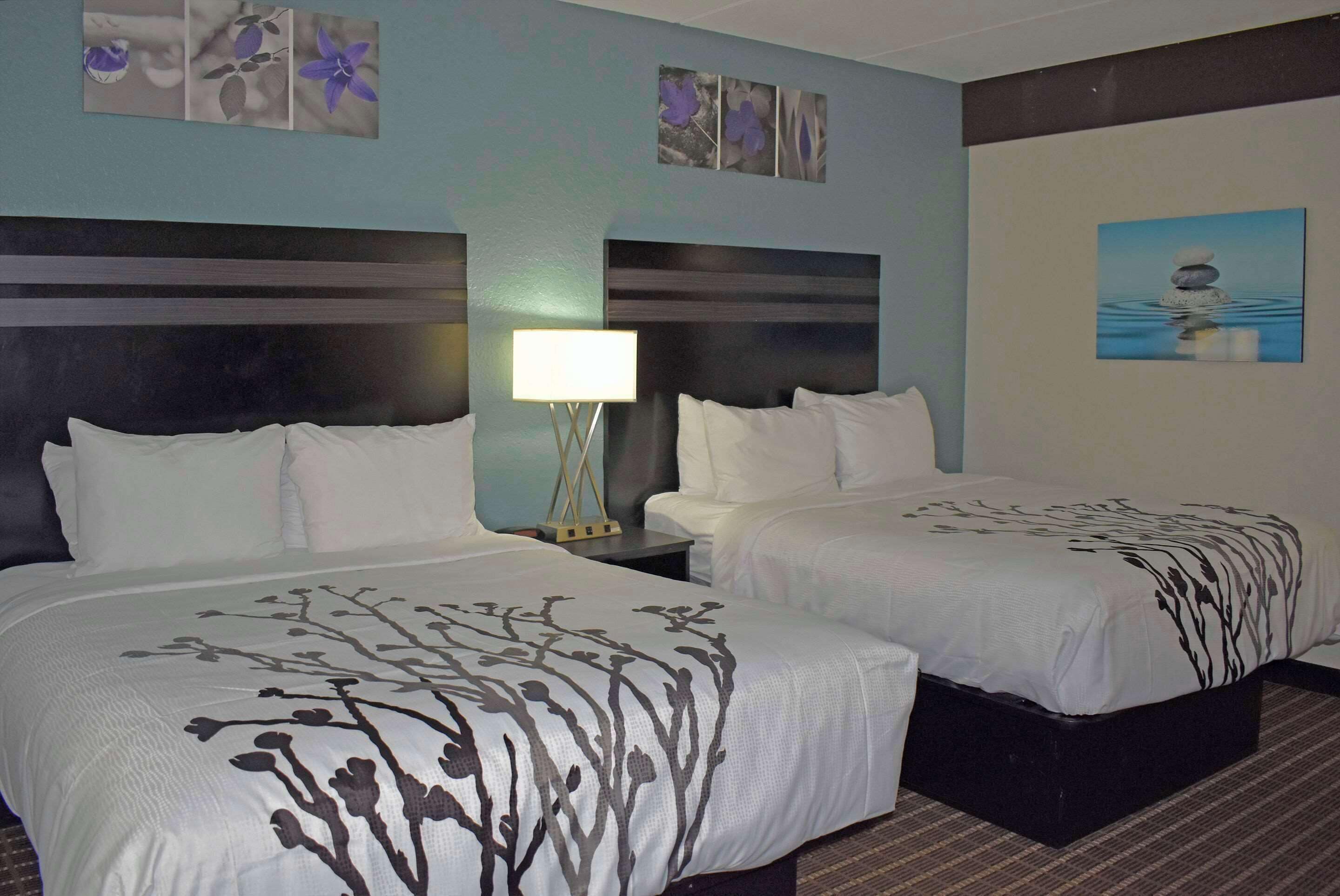 A hotel room with two beds, a nightstand with a lamp, and wall art.