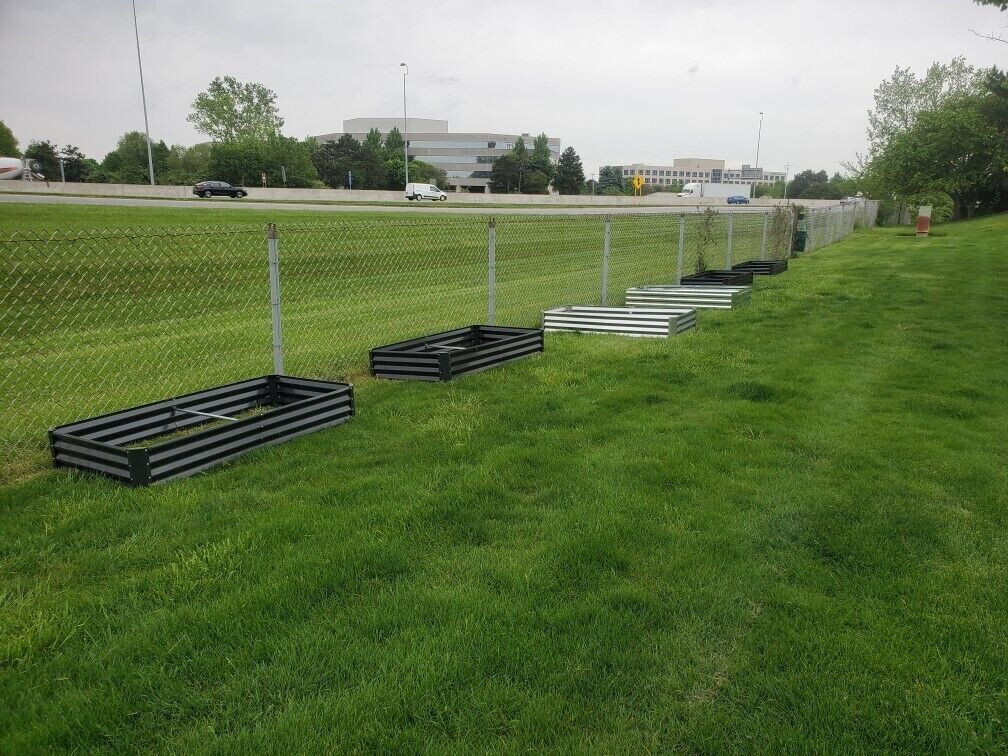 Un espacio cubierto de césped con estructuras metálicas, posiblemente para construcción o almacenamiento, y una carretera con vehículos al fondo.