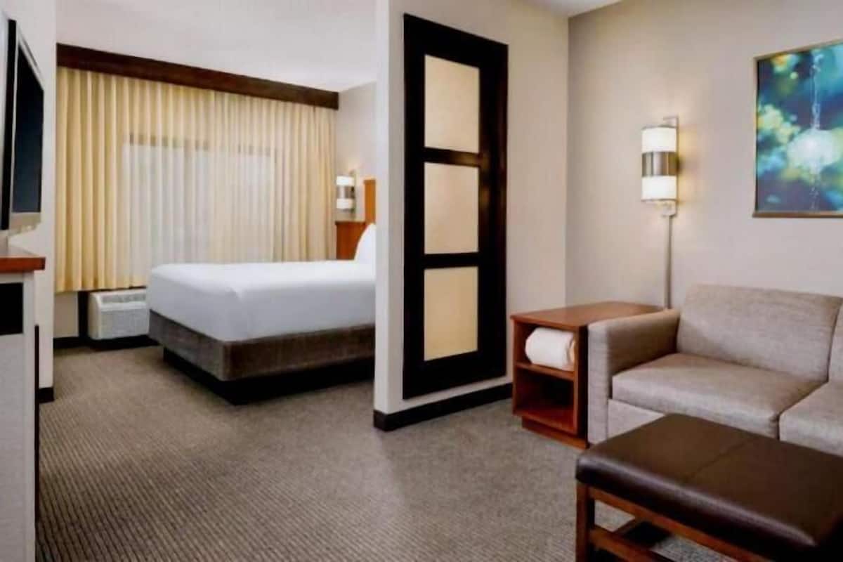 A hotel room with a bed, a sofa, a small table, a lamp, and a painting on the wall.