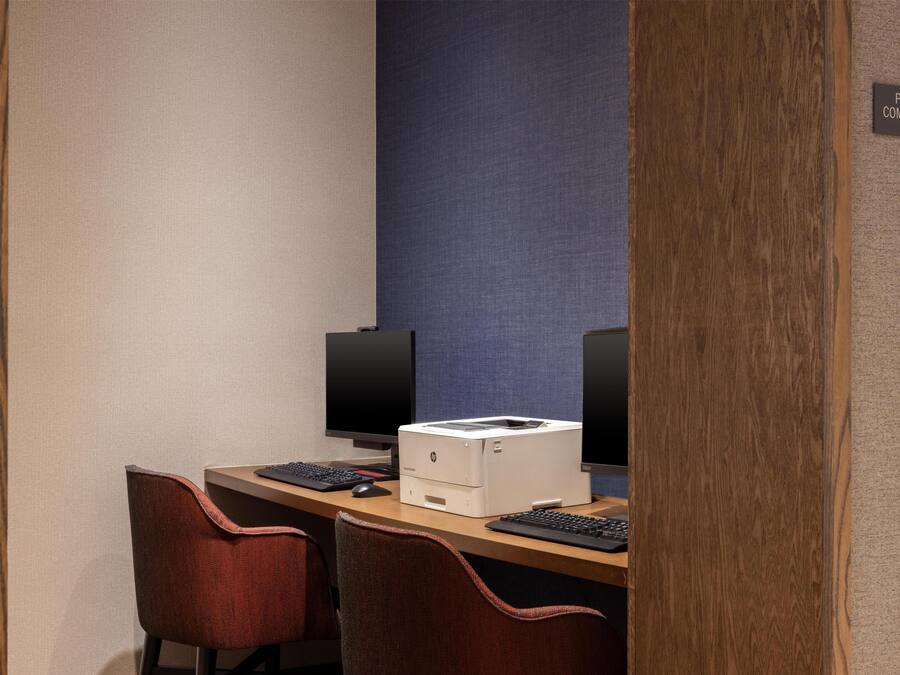 A hotel room with a desk, two chairs, a printer, and two monitors.