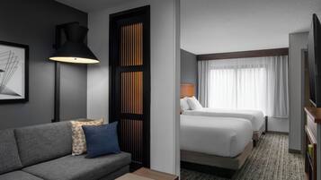 A hotel room with a gray sofa, two beds, a TV, and a framed picture on the wall.