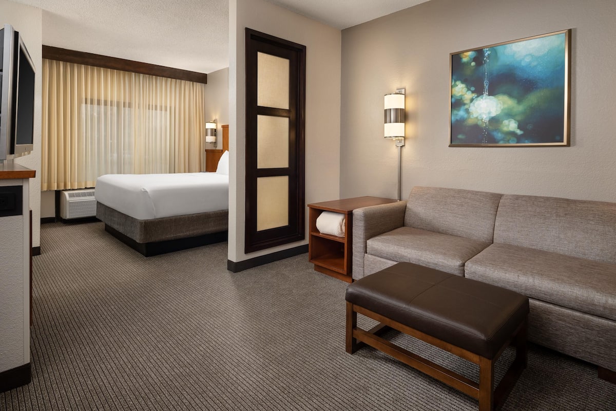 A hotel room with a bed, a sofa, a small table, a lamp, and a painting on the wall.