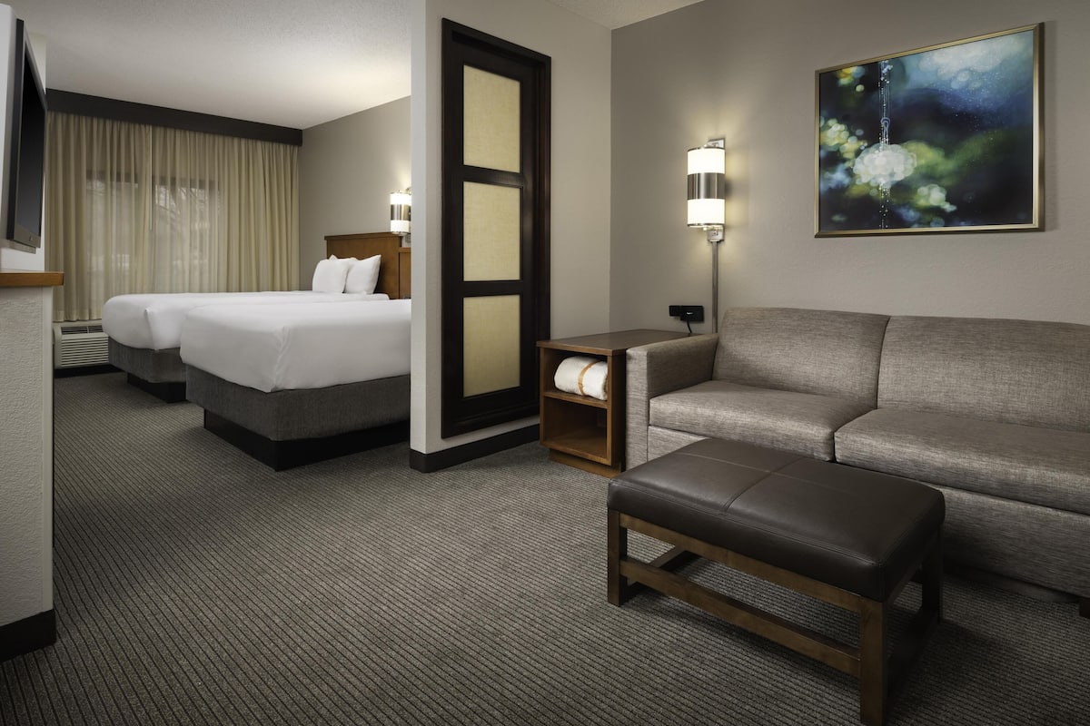 A hotel room with two beds, a sofa, a bench, a lamp, and a painting on the wall.