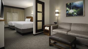 A hotel room with two beds, a sofa, a bench, a lamp, and a painting on the wall.