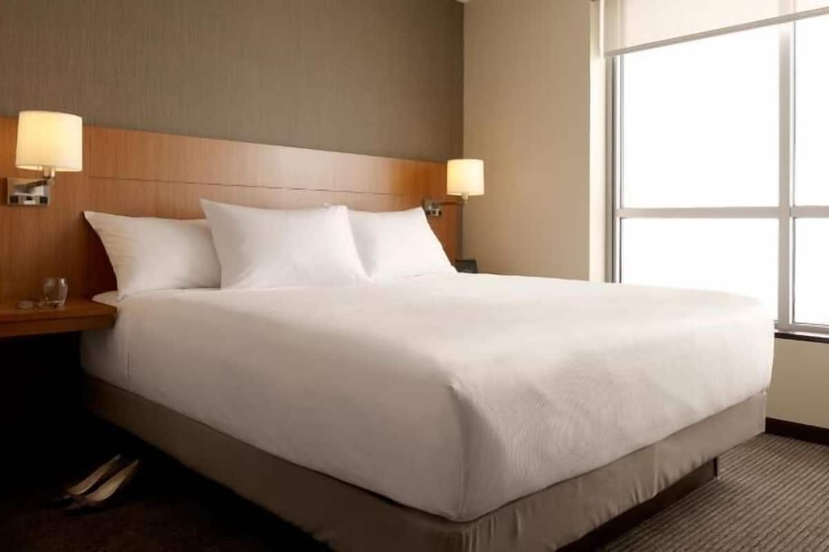 A hotel room with a large bed, two bedside lamps, a nightstand, and a window.