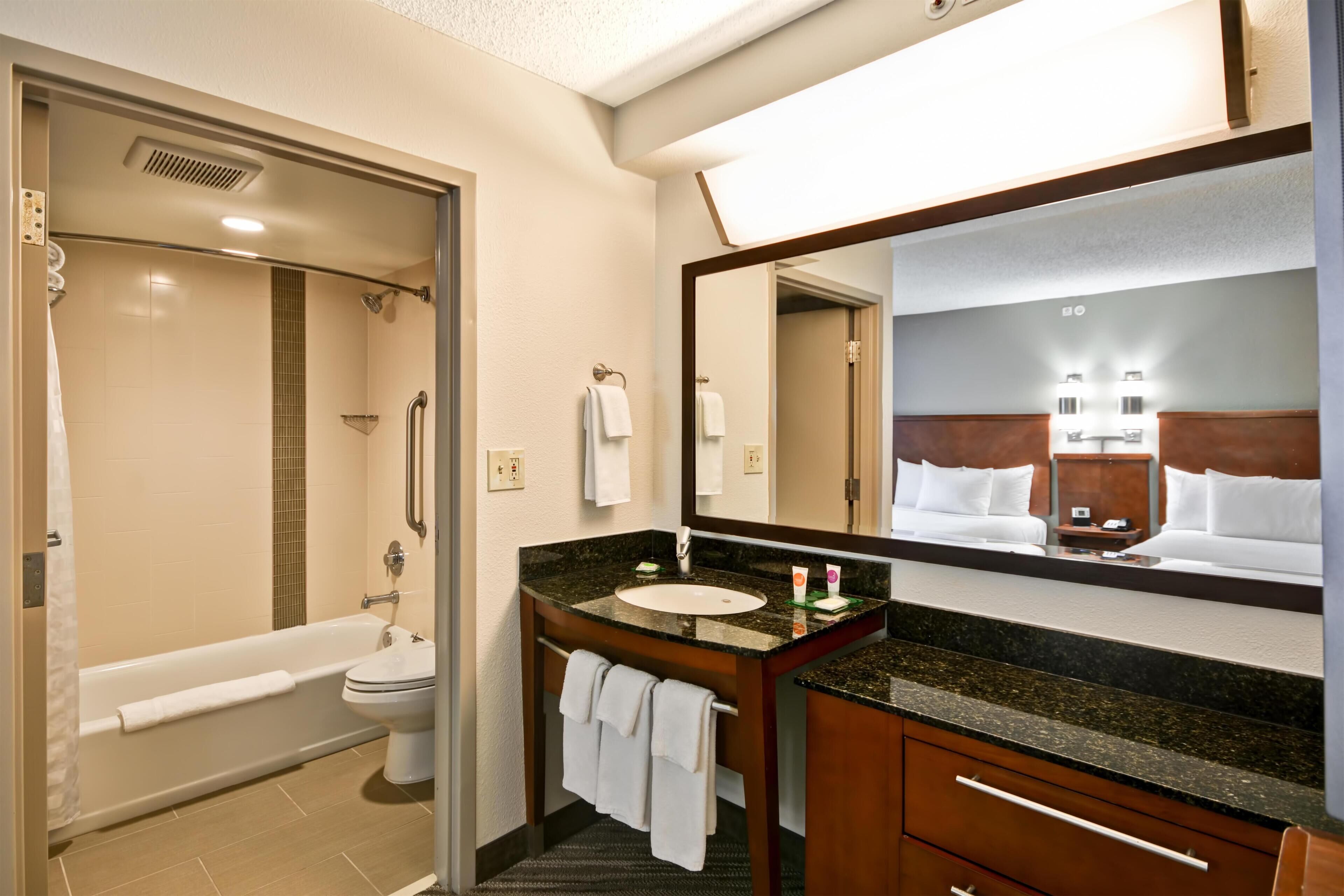 Un baño de hotel con bañera, inodoro, lavabo y un espejo grande.