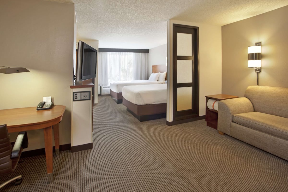A hotel room with a desk, two beds, a sofa, and a TV.