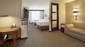 A hotel room with a desk, two beds, a sofa, and a TV.