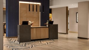 A reception area with a modern design, featuring a wooden reception desk, a blue accent wall, and hanging pendant lights. - Hyatt Place Columbus Dublin (Dublin)
