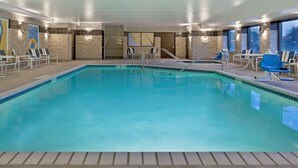 An indoor swimming pool with clear water, surrounded by lounge chairs and a tiled floor.