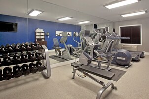 Un gimnasio con equipo de ejercicio, un espejo y una barra con mancuernas.