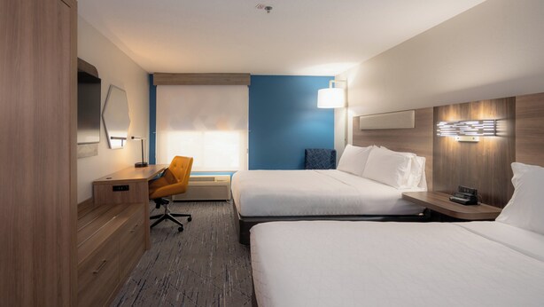 A hotel room with two beds, a desk, a chair, and a large window.