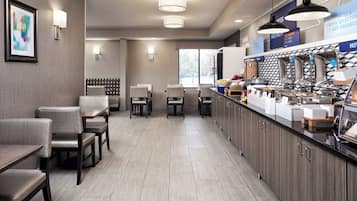 A modern hotel dining area with a long counter, multiple seating options, and a kitchen area with breakfast items.