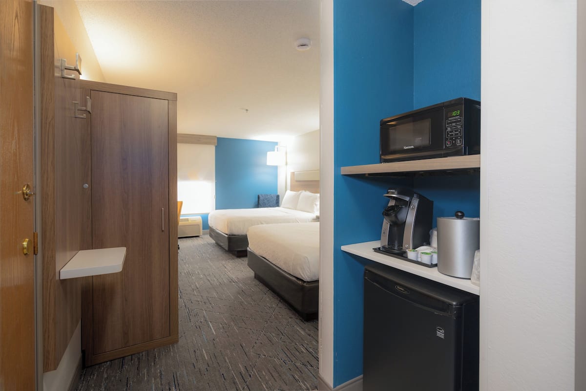 A hotel room with a wooden wardrobe, two beds, a microwave, a coffee maker, and a small refrigerator.