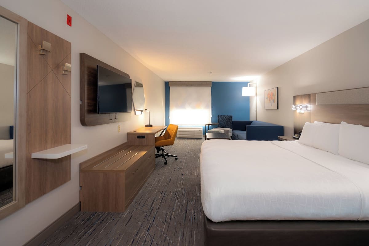 A hotel room with a large bed, a desk with a chair, a television, and a window with a view.