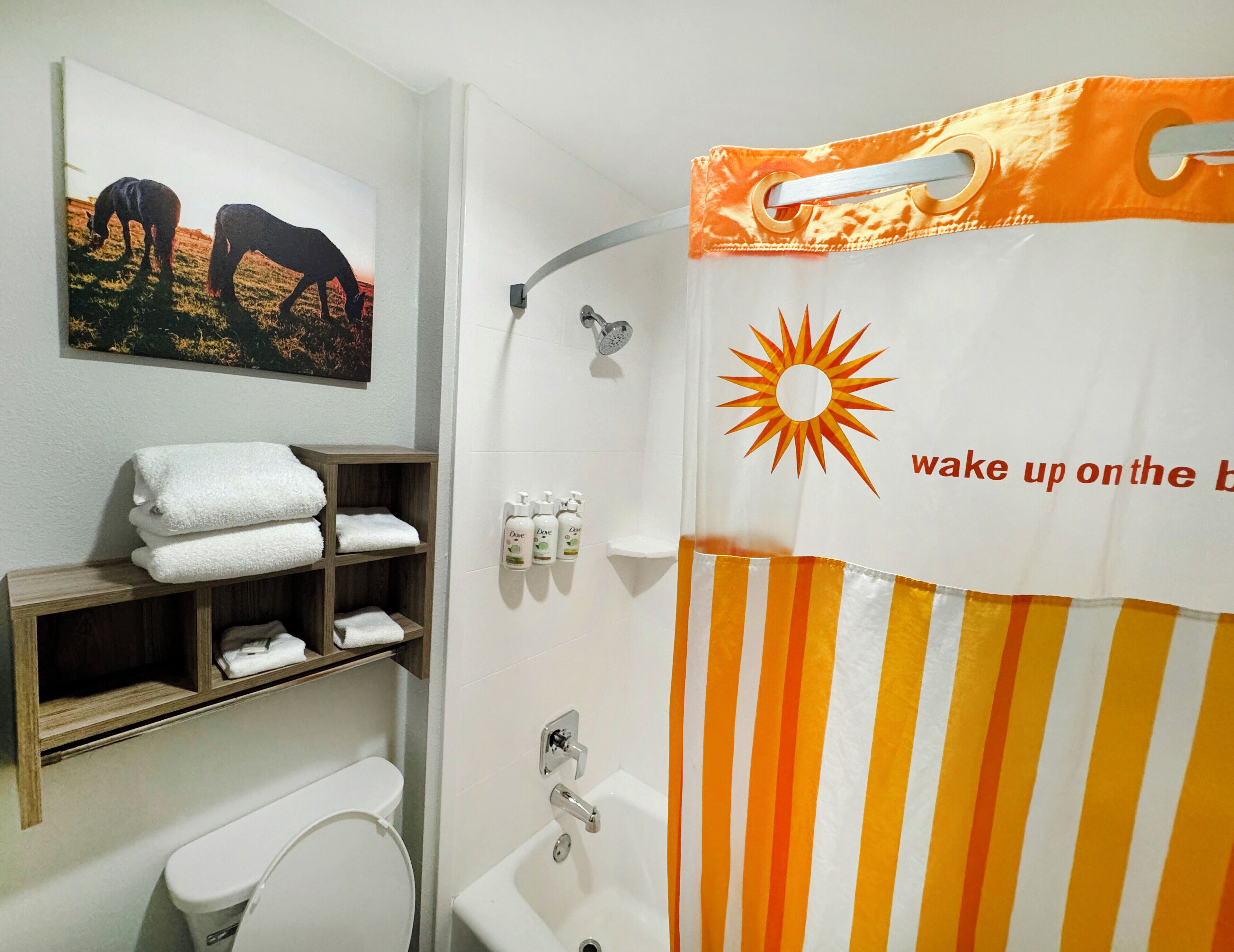 A bathroom with a shower curtain featuring a sun and text, a toilet, a sink, and a towel rack with folded towels.
