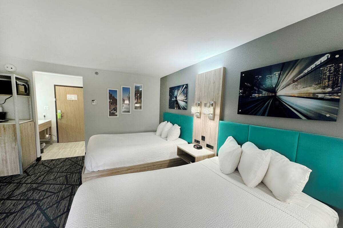 Una habitació d'hotel amb dos llits, una taula de treball, un mirall i obra d'art a les parets.