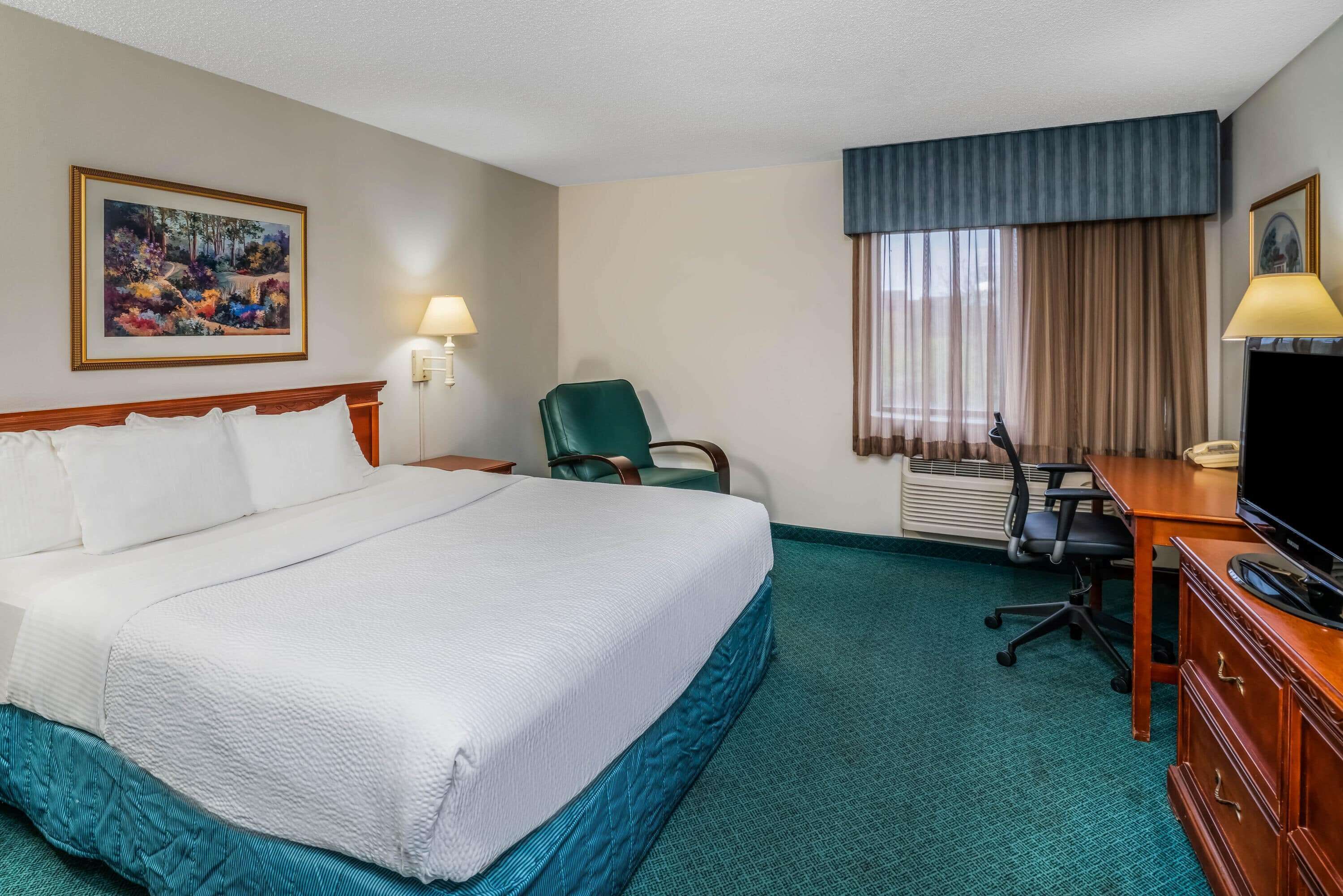 A hotel room with a large bed, a desk with a chair, a television, and a painting on the wall.