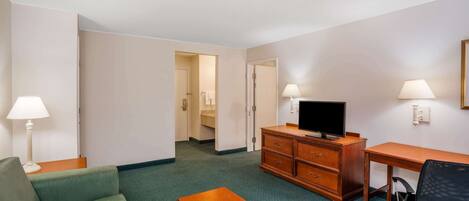 Habitación de hotel con un sofá verde, un escritorio de madera, un televisor y una silla.