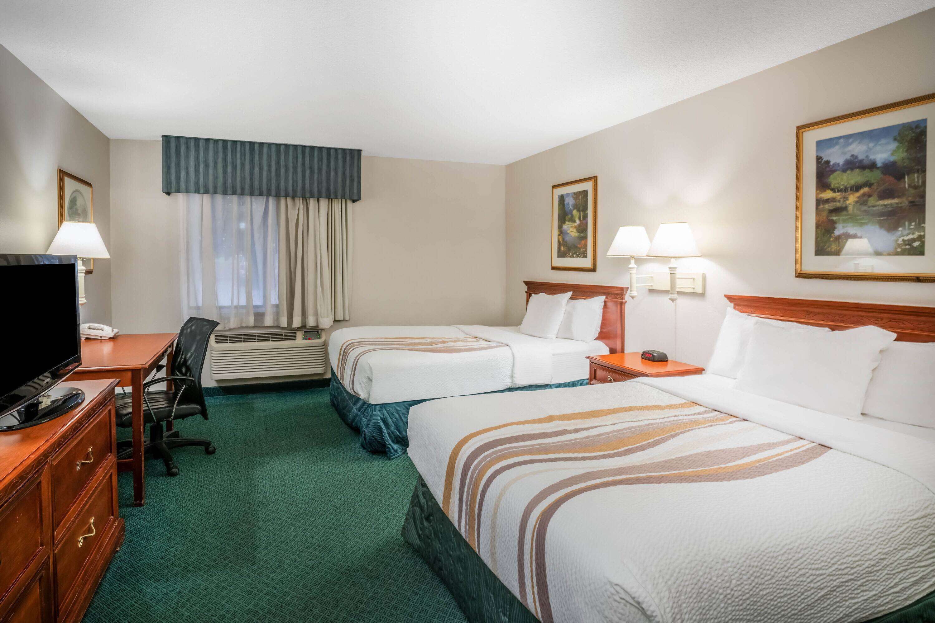 A hotel room with two beds, a desk, a TV, and a window with curtains.