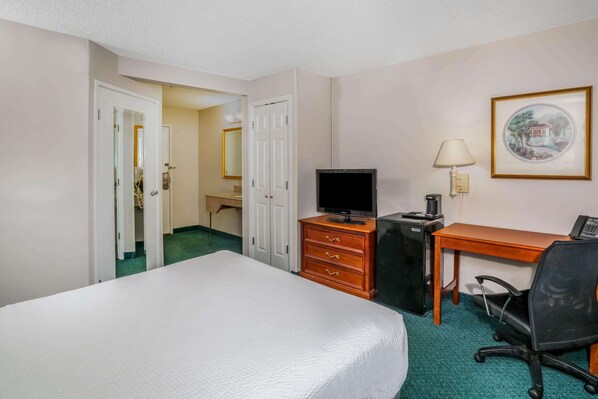 A hotel room with a bed, a desk, a chair, a television, and a desk lamp.