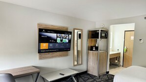 Habitación de hotel con televisión de pantalla plana montada en la pared, un escritorio, una silla, una cama y un armario.