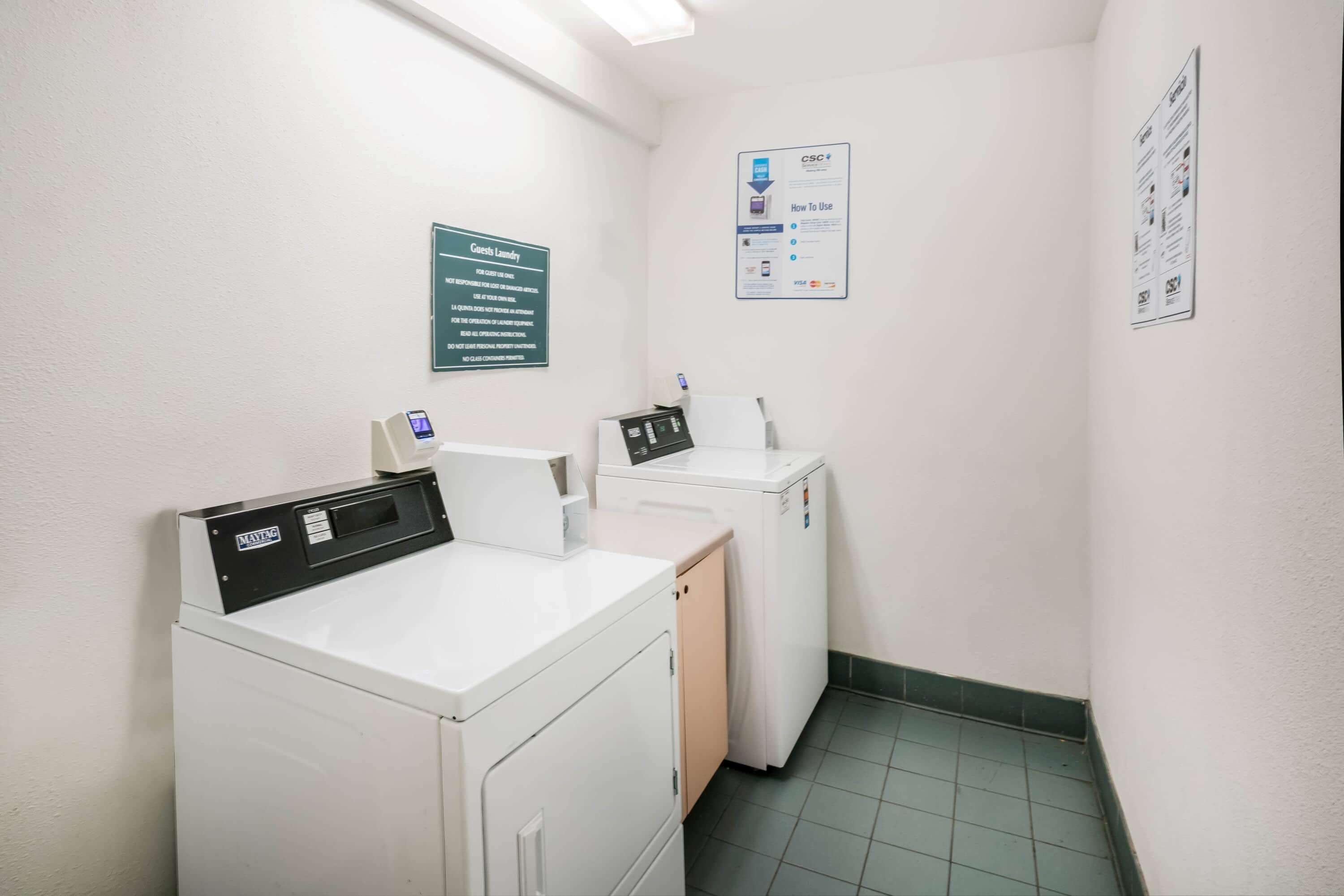 A laundry room with a front-loading washer and dryer, a control panel, and informational signs on the walls.