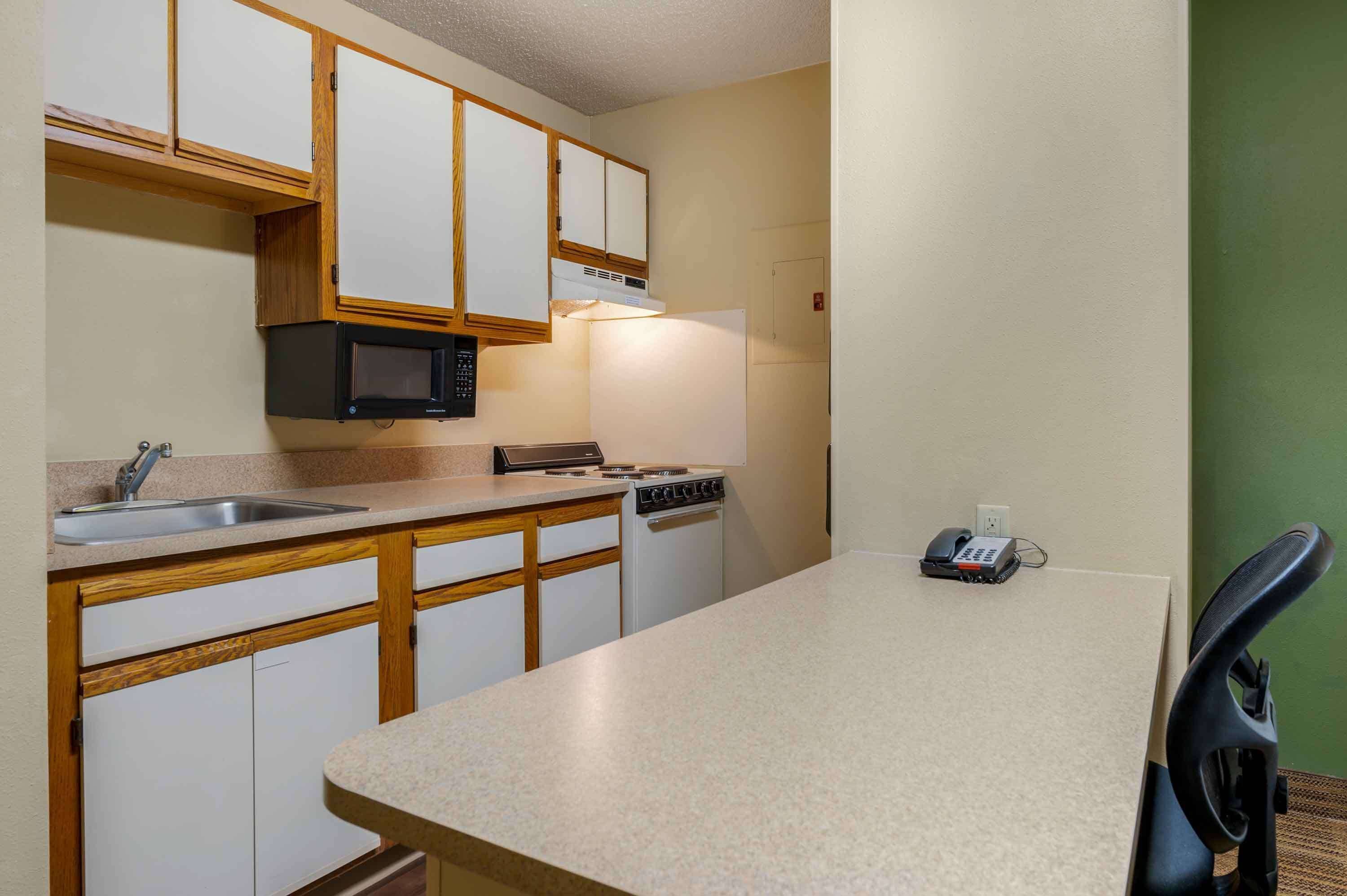 A compact kitchen with wooden cabinets, a microwave, a stove, and a sink.