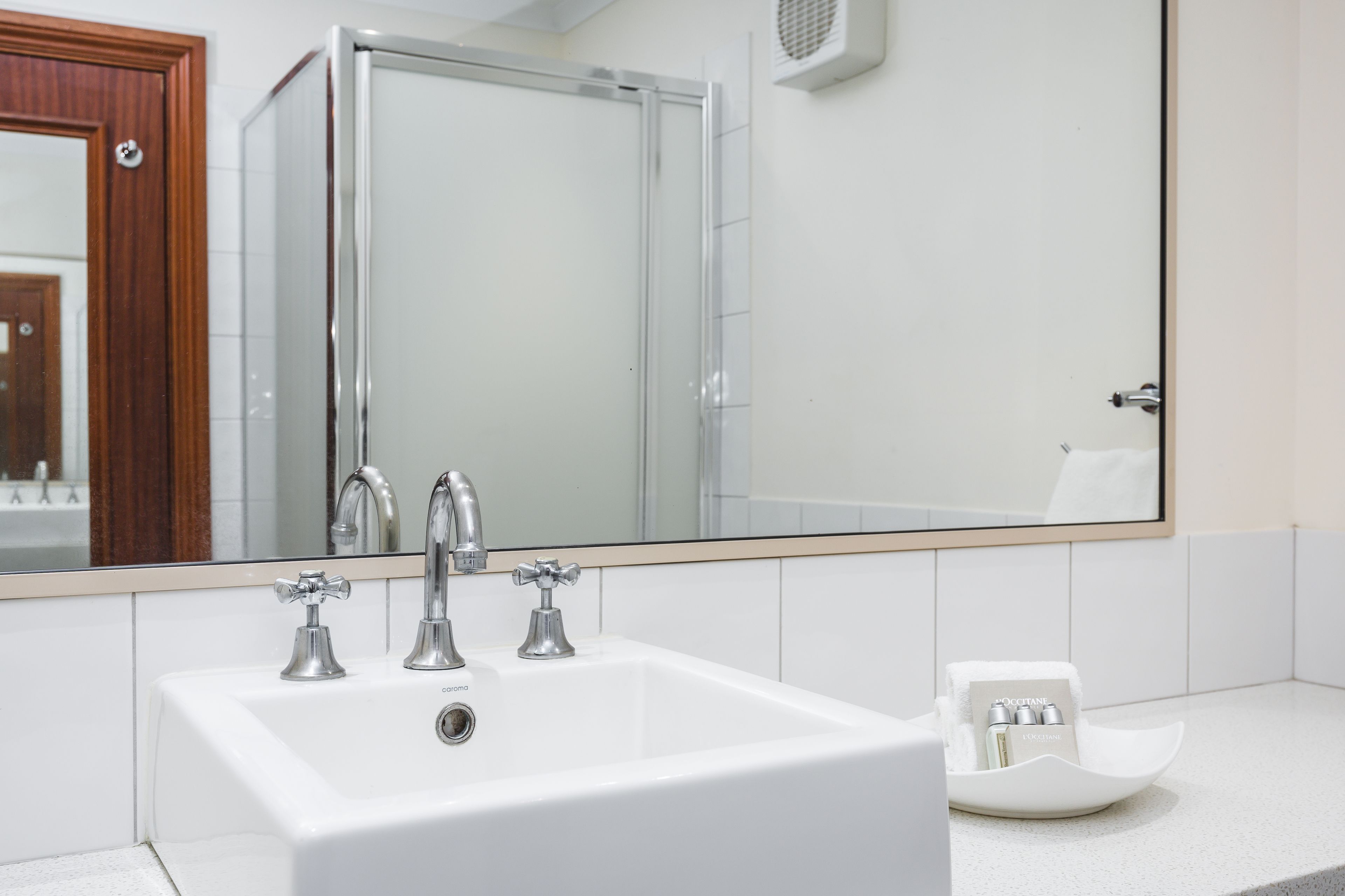 A bathroom with a white sink, two faucets, and a large mirror.