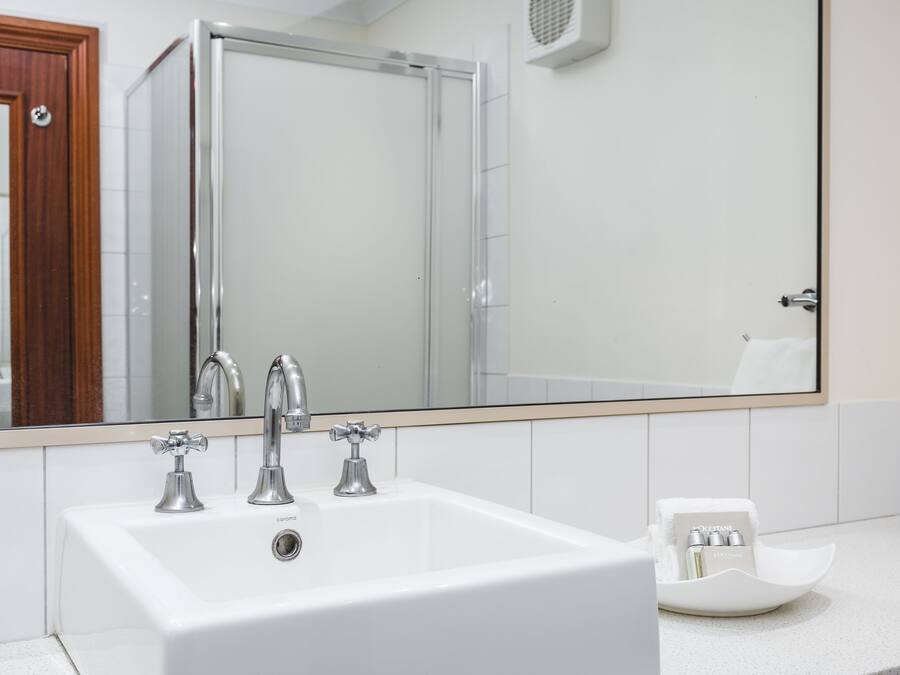Une salle de bain avec un lavabo blanc, deux robinets et un grand miroir.