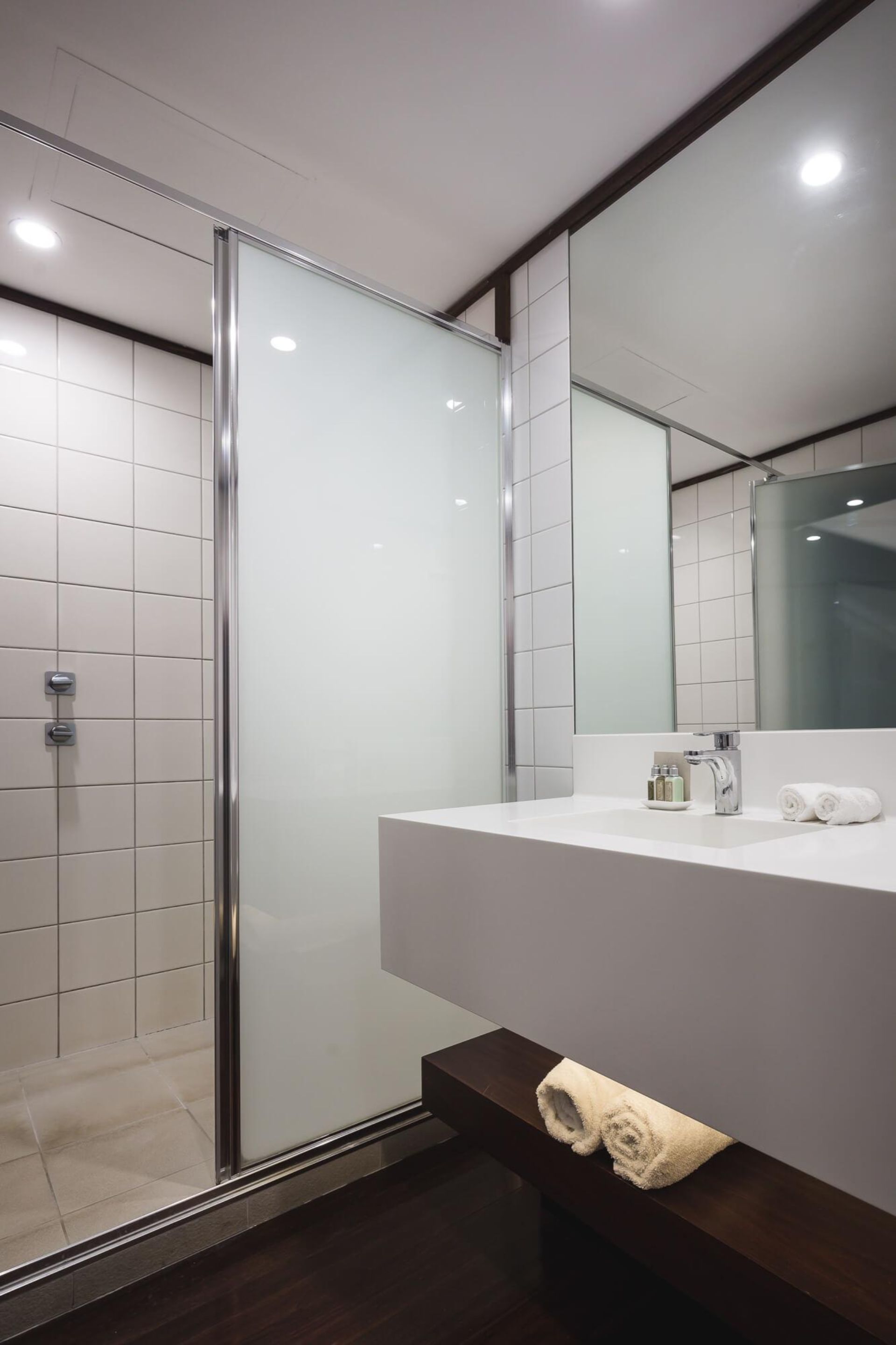A modern bathroom with a glass shower enclosure, a white sink with a mirror, and a towel rack.