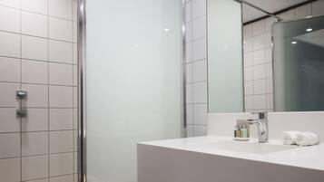 Un baño moderno con cabina de ducha de vidrio, un lavabo blanco con espejo y un perchero para toallas.