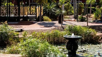 Un jardín con una fuente, palmeras y una estructura de madera.
