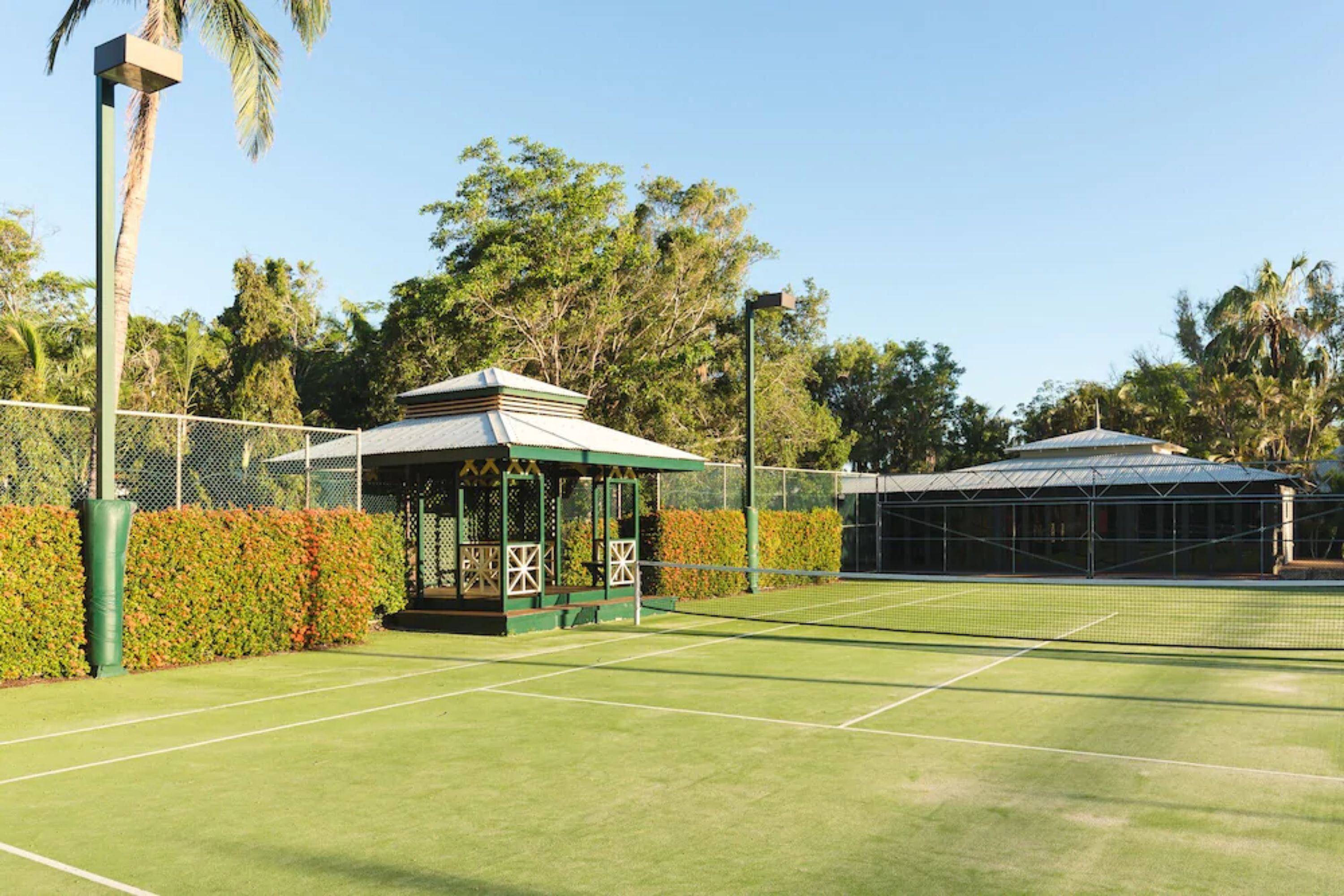 A tennis court with a pavilion, surrounded by a fence and trees.