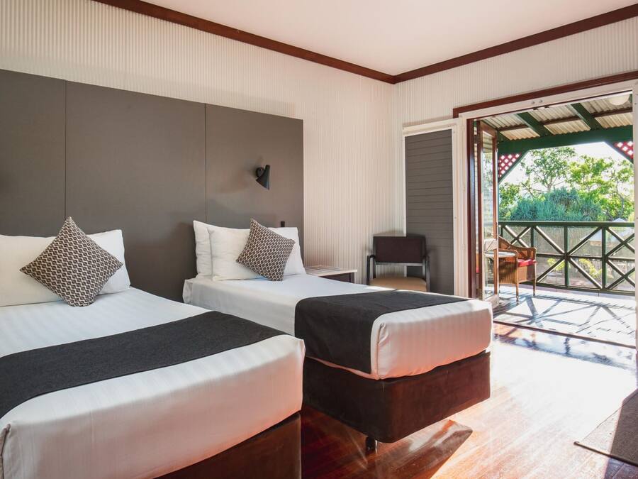A hotel room with two beds, a small table, and a view of the outdoors.
