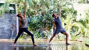 Two individuals performing yoga on a wooden deck with a lush green garden in the background. - Cable Beach Club Resort & Spa (Cable Beach)