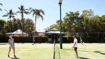 A tennis court with players, palm trees, and a gazebo in the background.