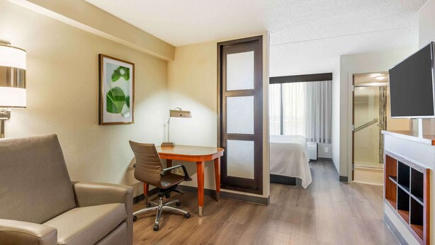 A hotel room with a sofa, a desk with a chair, a TV, and a bed.