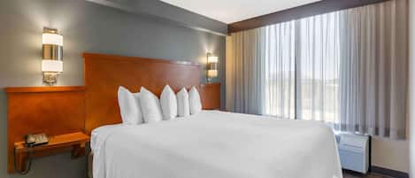 A hotel room with a large bed, two bedside tables with lamps, a telephone, and a window with curtains.