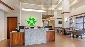 A reception area with a marble counter, wooden reception desk, and a green logo on the wall. - Extended Stay America Premier Suites - Cleveland - Independence (Independence)