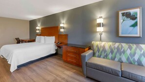A hotel room with a bed, a desk, a chair, a sofa, and two wall-mounted lamps.