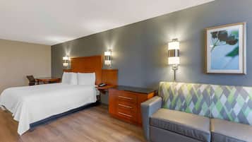 Habitación de hotel con cama, escritorio, sillón y dos lámparas de pared.