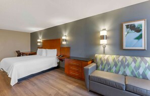 A hotel room with a bed, a desk, a chair, a sofa, and two wall-mounted lamps.