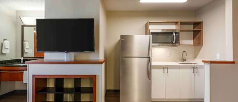 A modern kitchen with a flat-screen TV, stainless steel appliances, and wooden cabinetry.