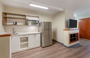 Una cocina compacta con microondas, refrigerador y estante empotrado para televisor.